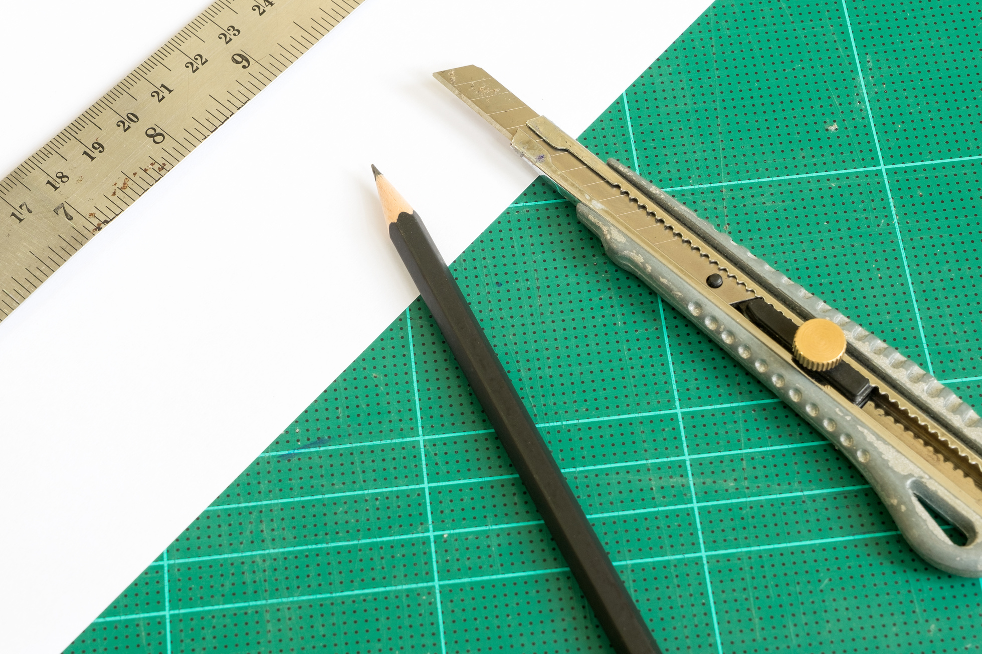 cutter and pencil with ruler on green cutting mat